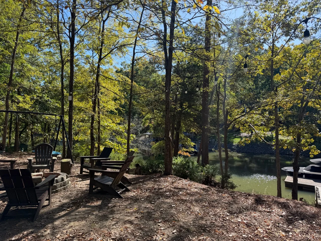 Chairs around a fire-pit area beneath trees beside the water